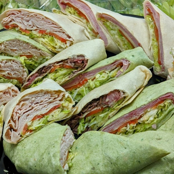 A platter of various deli meat wraps, including turkey, roast beef, and ham, with lettuce and tomato.