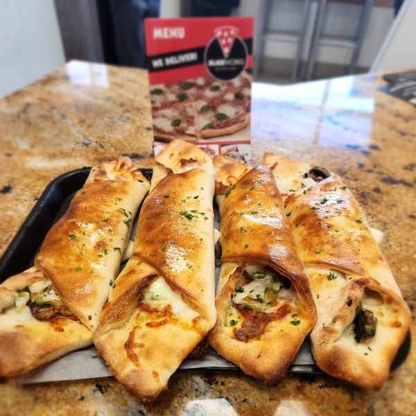 Golden-brown calzones filled with cheese and vegetables, garnished with parsley, on a black tray.