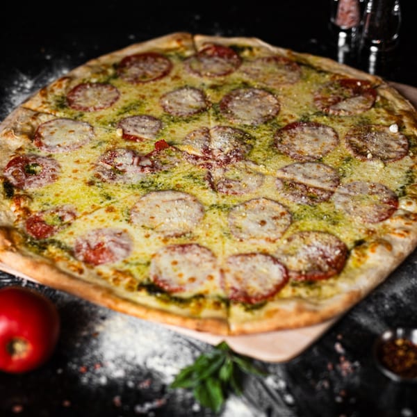 A whole pesto pizza from SliceWorks CT, topped with melted cheese and sliced tomatoes.