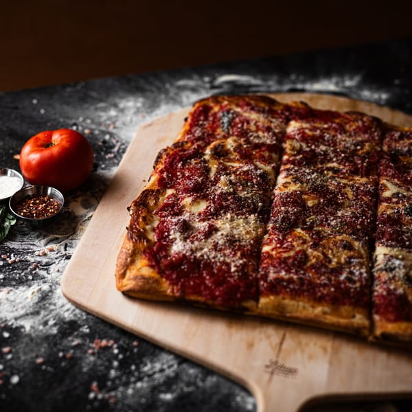 A rectangular SliceWorks CT pizza, topped with red sauce and cheese, on a wooden peel.