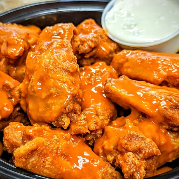 A close-up of buffalo wings from SliceWorks CT, coated in orange sauce, with a side of ranch.