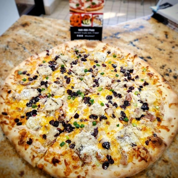 A white pizza from SliceWorks CT with cheese, dark toppings, and green onions on a granite counter.