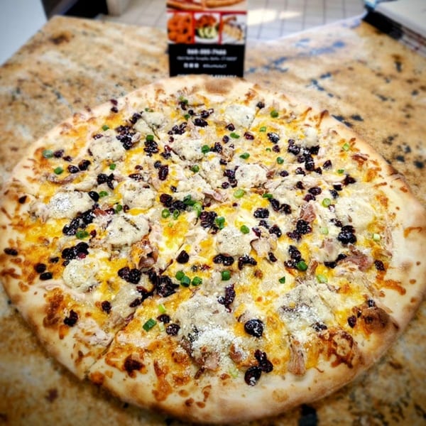A whole SliceWorks CT pizza with white sauce, cheese, dark toppings, and green onions.