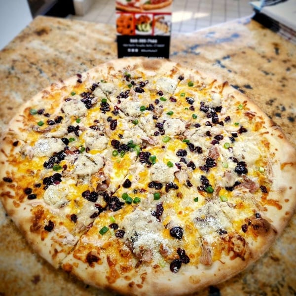 A SliceWorks CT pizza with white sauce, cheese, dark toppings, and green onions on a speckled counter.