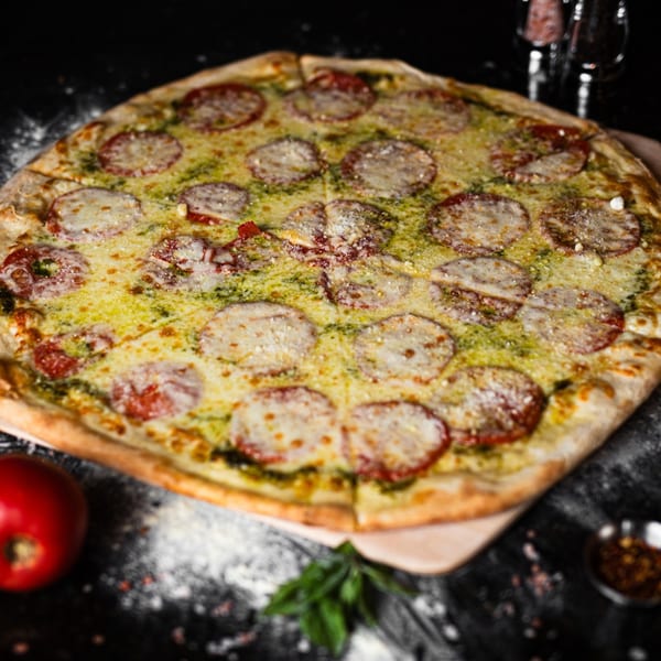 A SliceWorks CT pesto pizza with sliced tomatoes and mozzarella cheese on a dark surface.