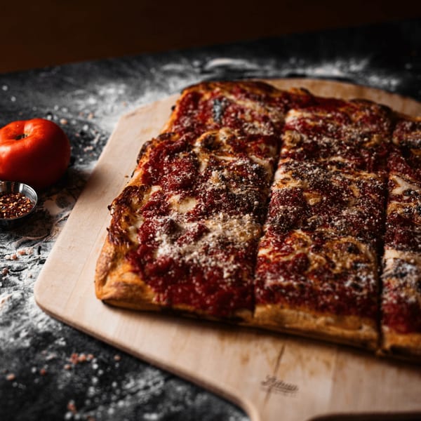 A rectangular SliceWorks CT pizza with red sauce and cheese, cut into slices on a wooden peel.