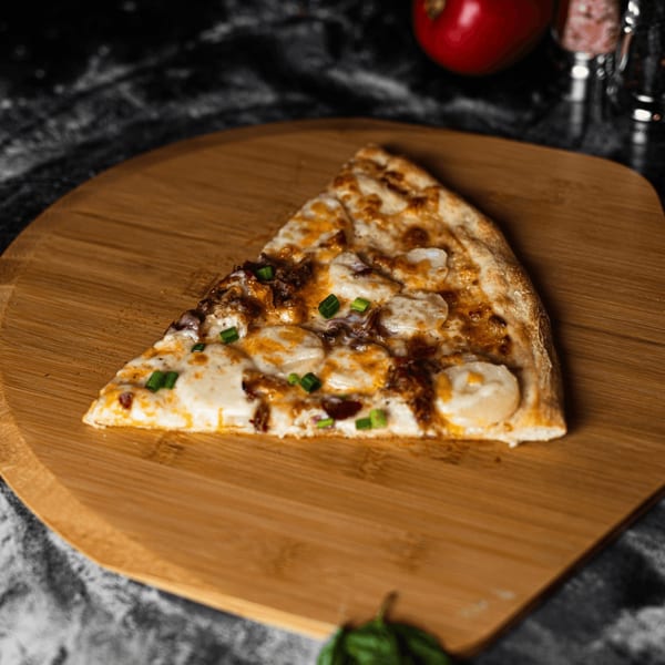 A SliceWorks CT pizza slice with white cheese and green onions on a wooden peel.
