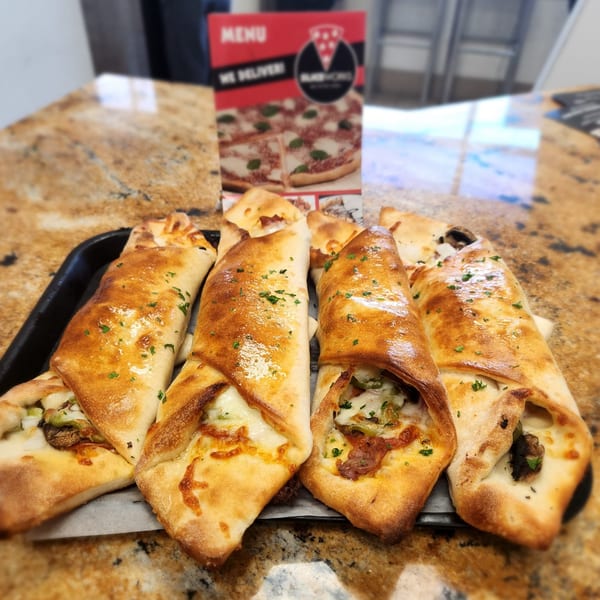 Golden-brown calzones filled with cheese and vegetables, garnished with parsley, on a black tray.