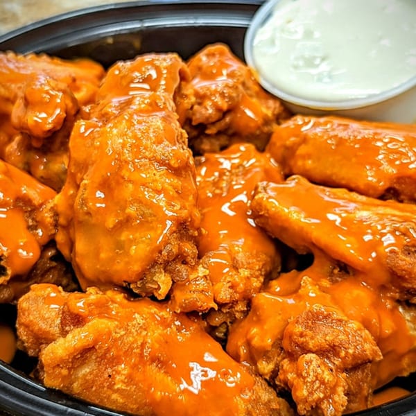 A close-up of buffalo wings from SliceWorks CT, coated in orange sauce with a side of ranch.
