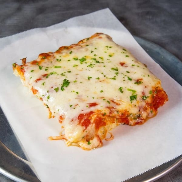 A cheesy SliceWorks CT pizza slice with melted mozzarella and parsley on white paper.